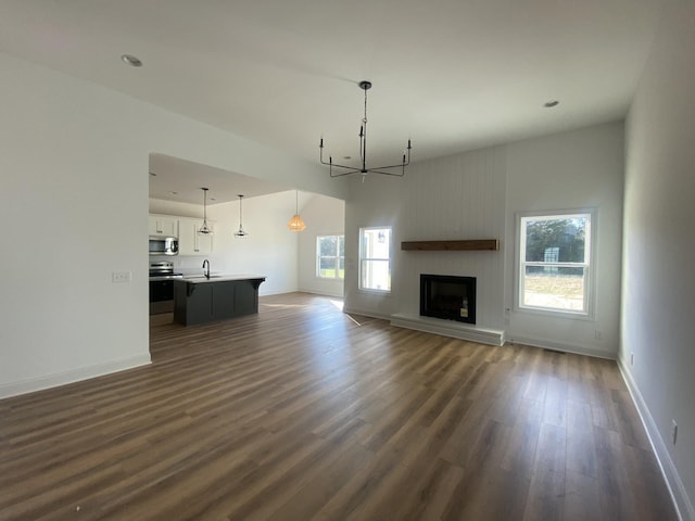 unfurnished living room with dark wood finished floors, a fireplace with raised hearth, baseboards, and a sink