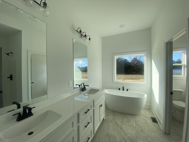 bathroom featuring toilet, a freestanding tub, plenty of natural light, marble finish floor, and a sink