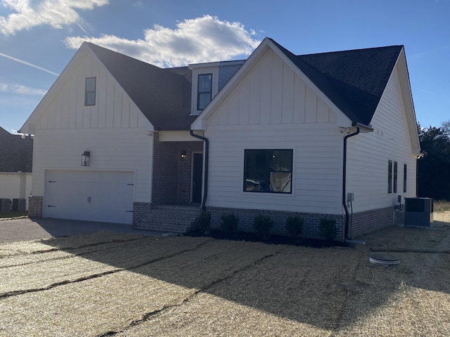 modern farmhouse featuring gravel driveway, brick siding, central AC, a garage, and board and batten siding