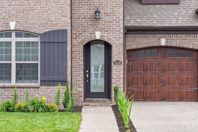 entrance to property featuring brick siding, a shingled roof, and a garage