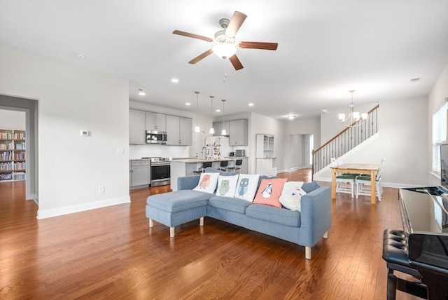 living area with ceiling fan with notable chandelier, wood finished floors, recessed lighting, baseboards, and stairs