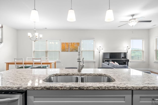 kitchen with light stone counters, gray cabinetry, a sink, ceiling fan with notable chandelier, and open floor plan