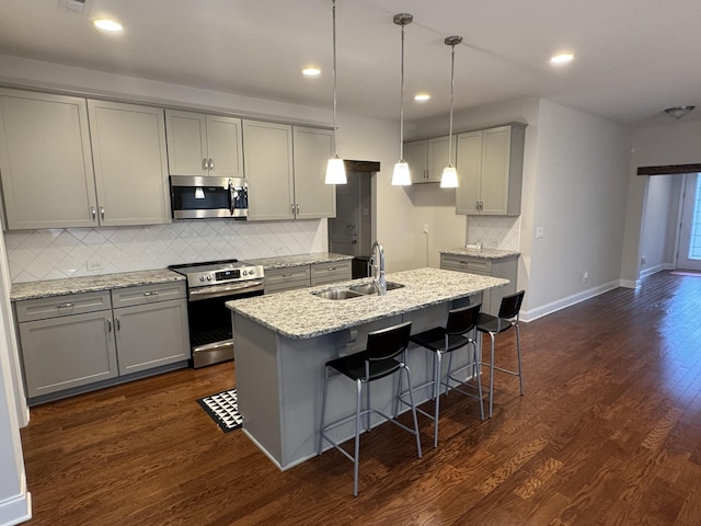 kitchen featuring dark wood-style floors, a center island with sink, a sink, gray cabinetry, and appliances with stainless steel finishes