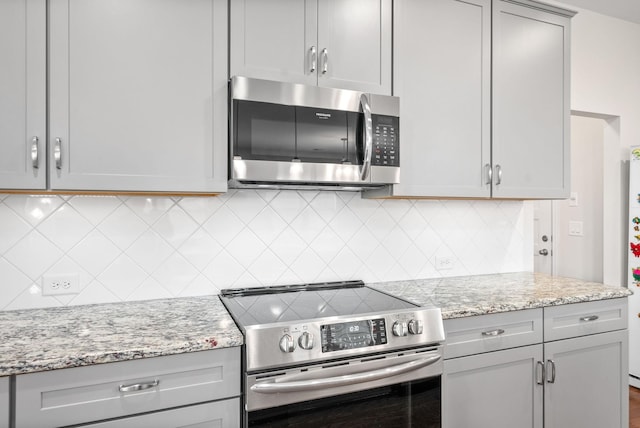 kitchen featuring light stone counters, stainless steel appliances, decorative backsplash, and gray cabinets