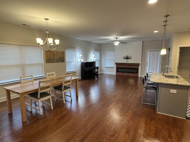 dining area with visible vents, dark wood-type flooring, baseboards, ceiling fan with notable chandelier, and a fireplace