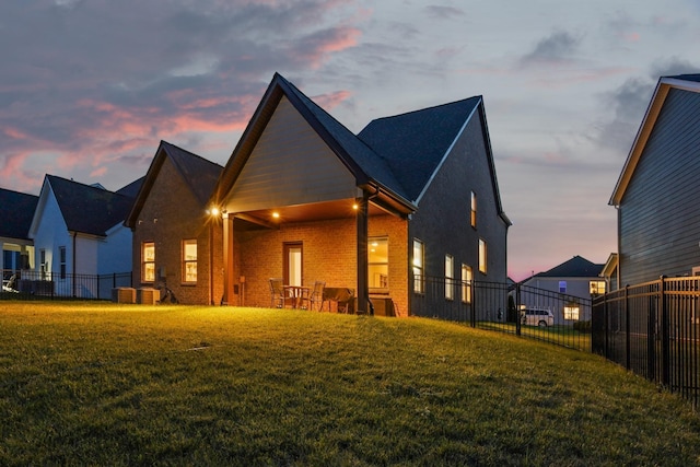 back of property at dusk with brick siding, a fenced backyard, and a yard