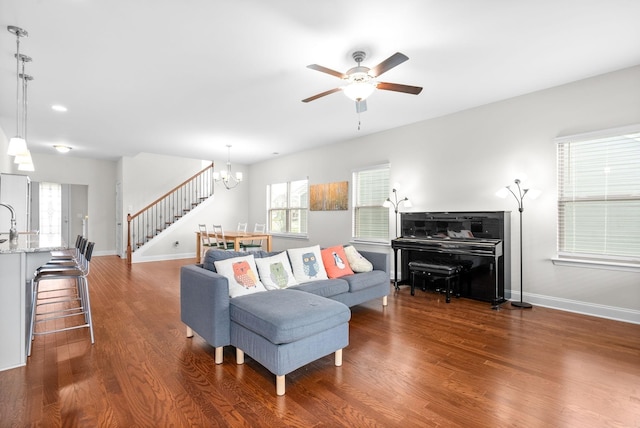 living room featuring ceiling fan with notable chandelier, wood finished floors, and baseboards