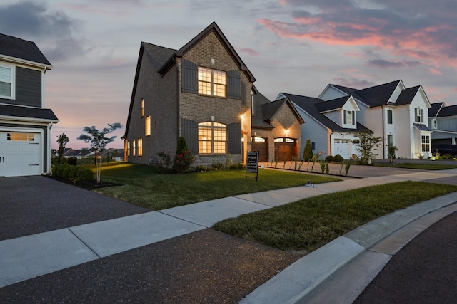 view of front facade featuring aphalt driveway, brick siding, a garage, and a yard