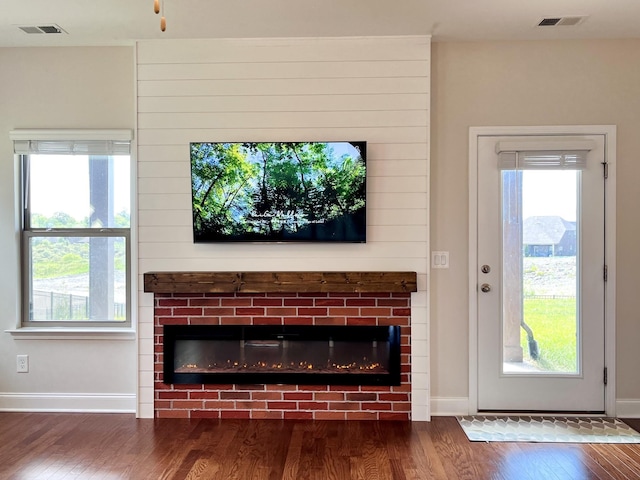 unfurnished living room featuring visible vents, a brick fireplace, and wood finished floors