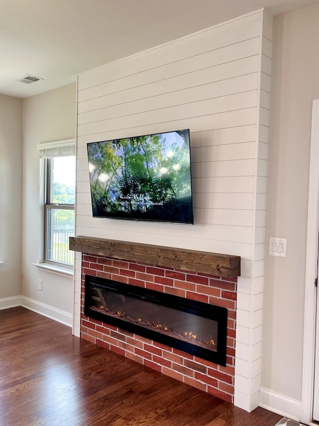 room details with visible vents, baseboards, a brick fireplace, and wood finished floors