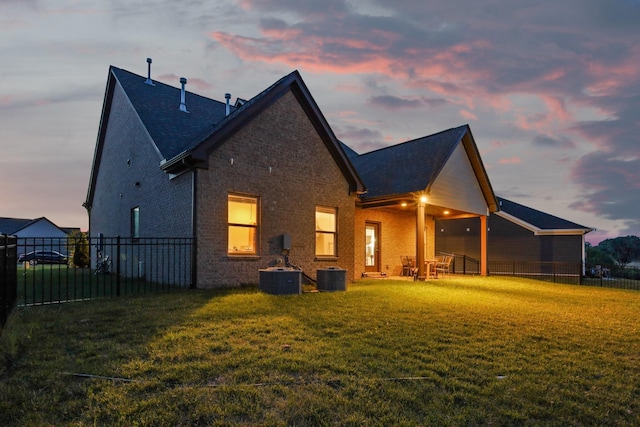 back of property at dusk with a yard, fence, brick siding, and central AC