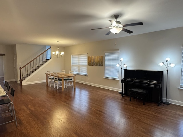 dining area featuring stairway, ceiling fan with notable chandelier, dark wood-type flooring, and baseboards