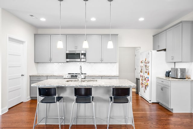 kitchen with stainless steel microwave, gray cabinetry, dark wood-type flooring, and a kitchen island with sink