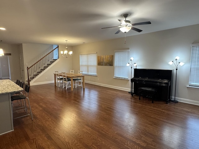 unfurnished living room featuring baseboards, dark wood-style floors, stairs, and ceiling fan with notable chandelier