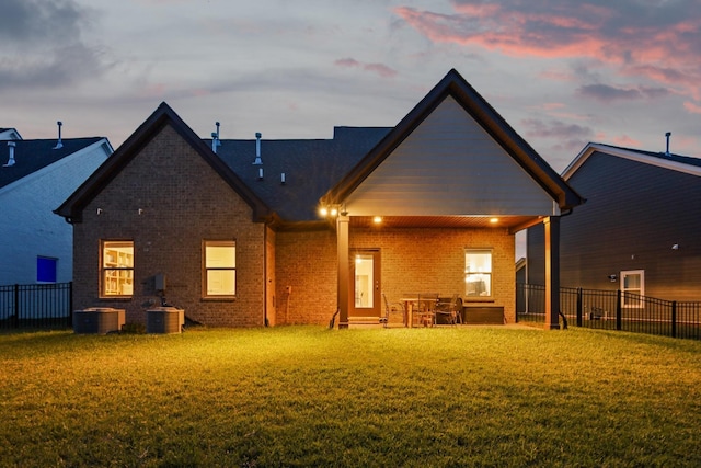 back of house at dusk with brick siding, central AC, a yard, and fence