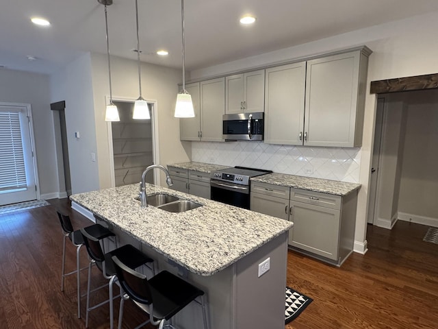 kitchen featuring dark wood-type flooring, gray cabinets, a sink, stainless steel appliances, and light stone countertops