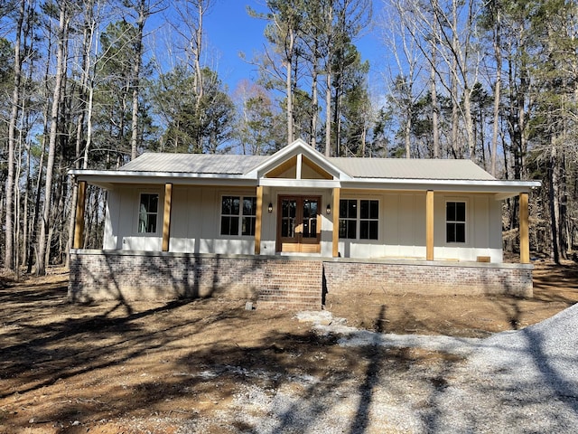 view of front facade with brick siding, covered porch, board and batten siding, and french doors