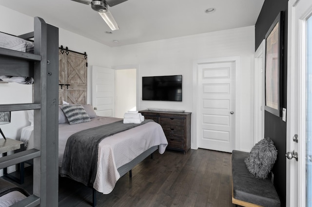 bedroom with a barn door, a ceiling fan, and dark wood-style flooring