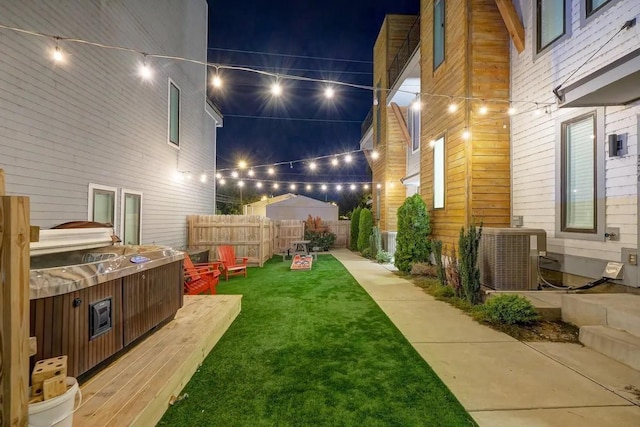 yard at night featuring central air condition unit, fence, and a hot tub