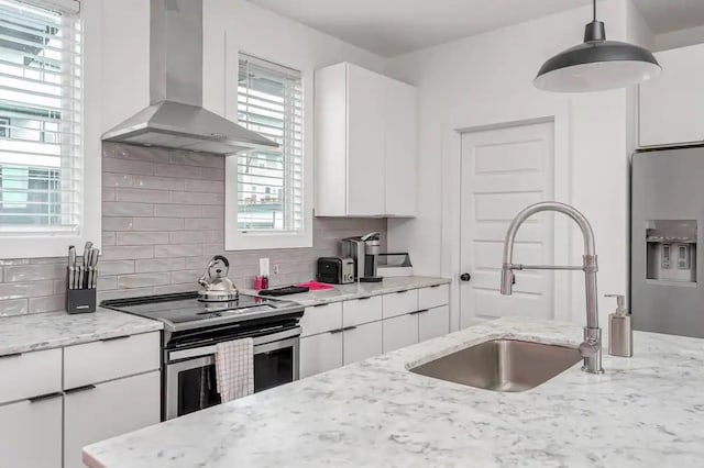 kitchen with tasteful backsplash, wall chimney range hood, white cabinets, stainless steel appliances, and a sink