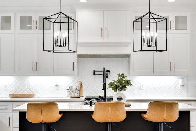 kitchen with light countertops, a kitchen breakfast bar, glass insert cabinets, and white cabinets