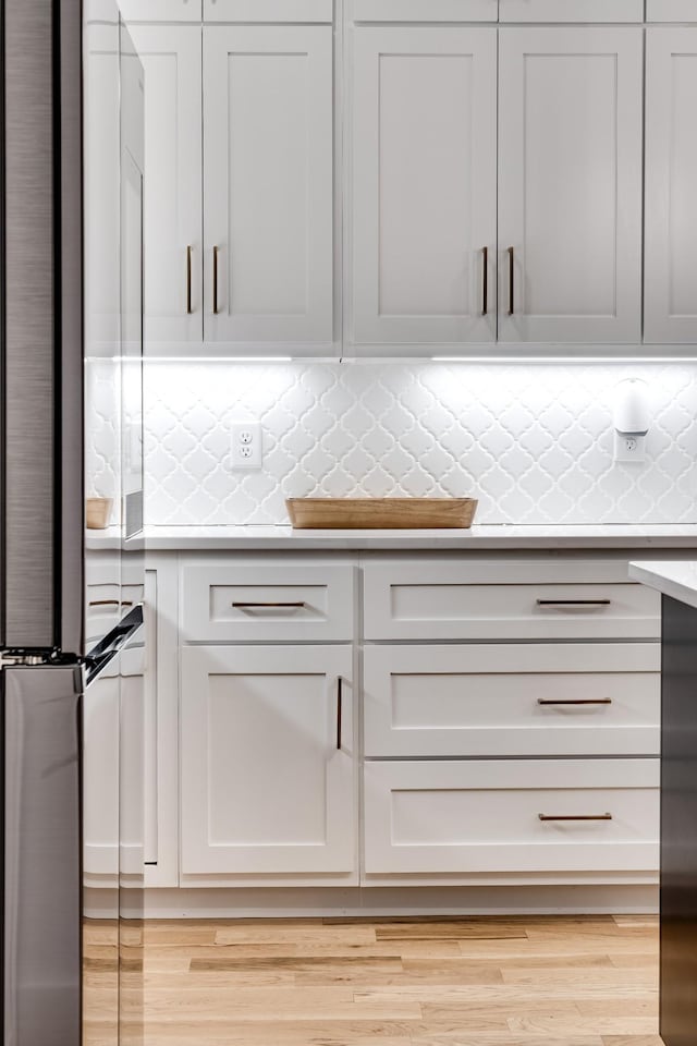 kitchen featuring light wood-style floors, stainless steel fridge, backsplash, and light countertops