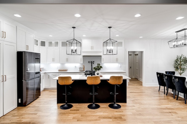 kitchen featuring white cabinetry, a kitchen island with sink, light countertops, and freestanding refrigerator