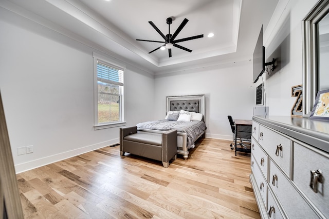 bedroom with light wood-style flooring, a raised ceiling, and baseboards