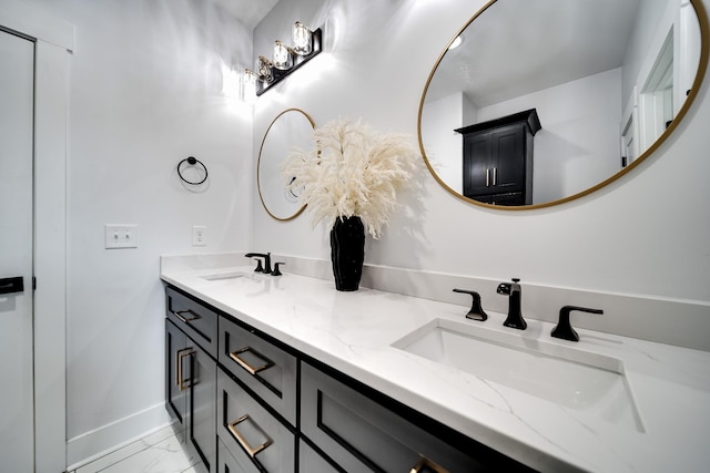 full bath featuring double vanity, marble finish floor, baseboards, and a sink