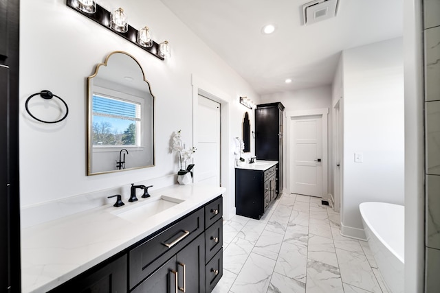 full bathroom with two vanities, recessed lighting, a freestanding bath, a sink, and marble finish floor