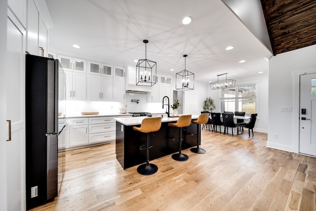 kitchen featuring backsplash, light countertops, light wood-style flooring, a kitchen breakfast bar, and freestanding refrigerator