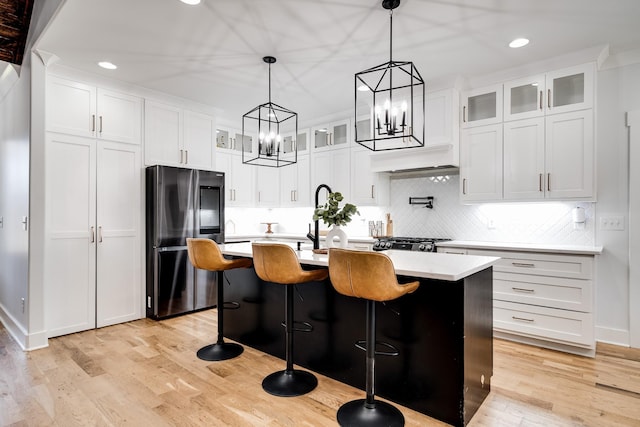 kitchen with a center island with sink, smart refrigerator, white cabinets, light wood finished floors, and light countertops