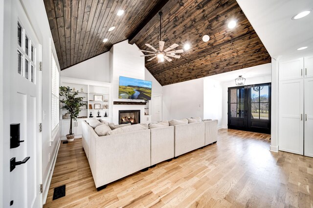 living room featuring beamed ceiling, built in features, a warm lit fireplace, wooden ceiling, and light wood-style floors