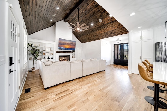 living area with beamed ceiling, light wood-type flooring, wooden ceiling, a warm lit fireplace, and french doors