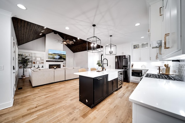 kitchen featuring light wood-style flooring, a warm lit fireplace, a sink, black appliances, and light countertops