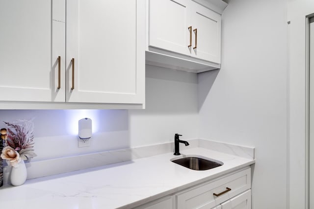 kitchen featuring a sink, light stone counters, and white cabinetry