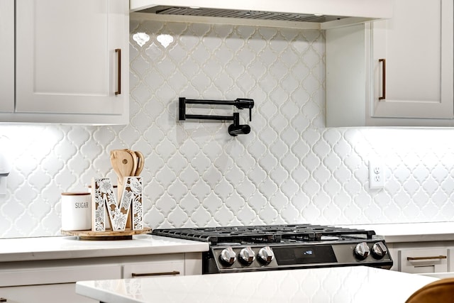 kitchen with stainless steel gas range oven, light stone counters, backsplash, and white cabinets