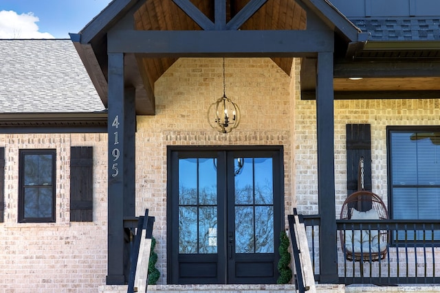 entrance to property with french doors, brick siding, and a shingled roof