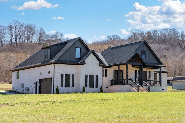 back of house featuring brick siding, covered porch, a lawn, and roof with shingles