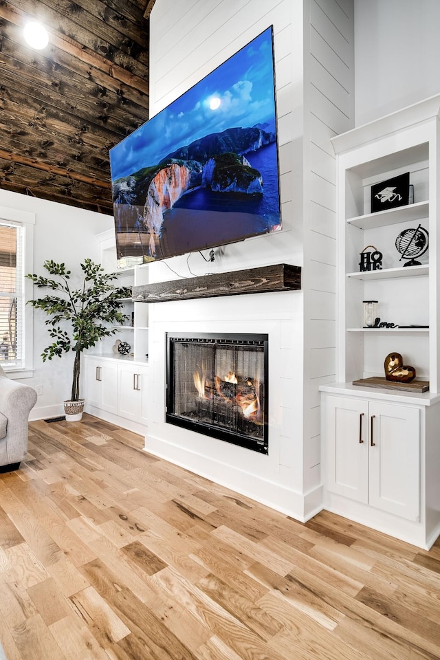 unfurnished living room with baseboards, light wood-type flooring, and a lit fireplace