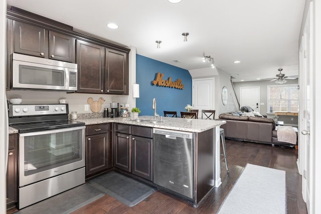 kitchen featuring a peninsula, a sink, dark brown cabinetry, appliances with stainless steel finishes, and open floor plan