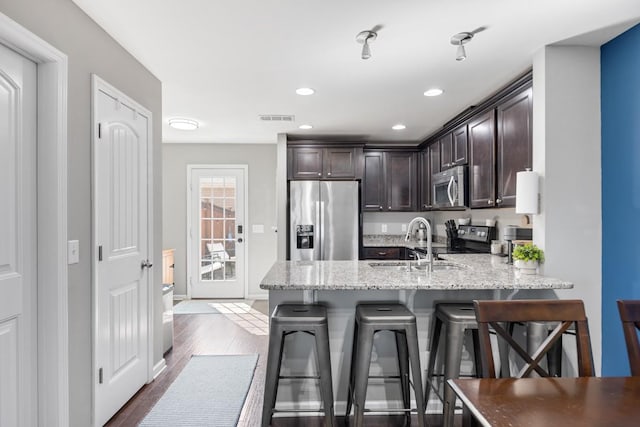 kitchen with visible vents, a peninsula, dark brown cabinetry, appliances with stainless steel finishes, and a kitchen breakfast bar