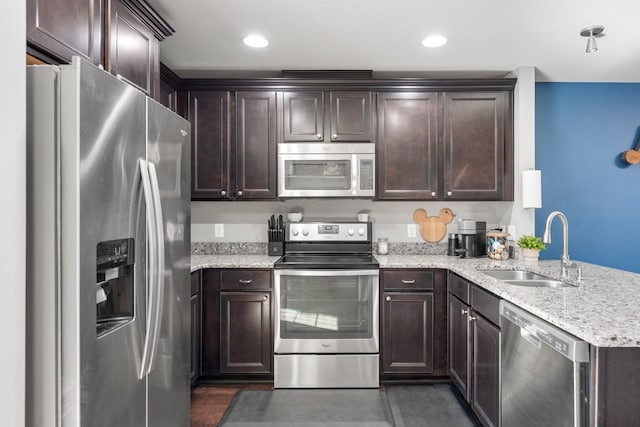 kitchen featuring light stone countertops, dark brown cabinetry, appliances with stainless steel finishes, a peninsula, and a sink