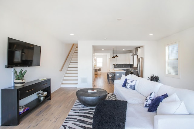 living area with visible vents, baseboards, stairs, light wood-type flooring, and recessed lighting