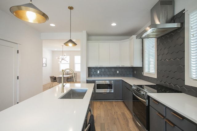 kitchen featuring a sink, appliances with stainless steel finishes, exhaust hood, light wood finished floors, and light countertops