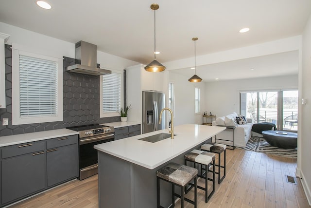 kitchen with a breakfast bar area, a sink, light wood-style floors, appliances with stainless steel finishes, and wall chimney exhaust hood