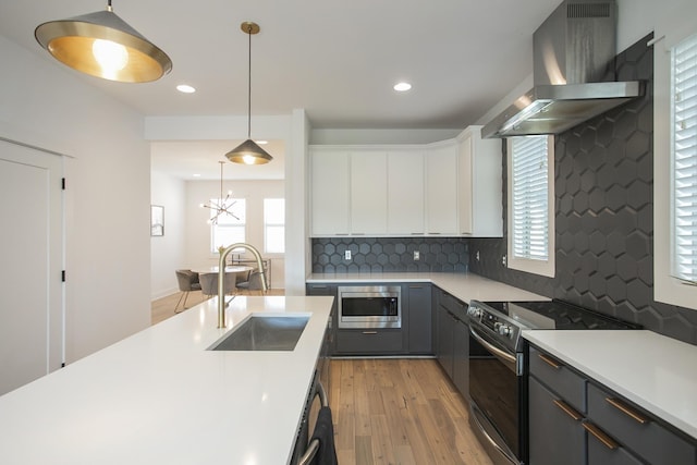 kitchen featuring light wood-type flooring, a sink, range hood, appliances with stainless steel finishes, and light countertops