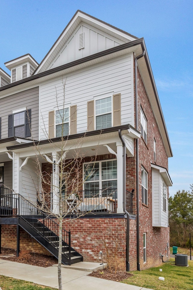 multi unit property featuring brick siding, board and batten siding, stairs, central AC unit, and covered porch