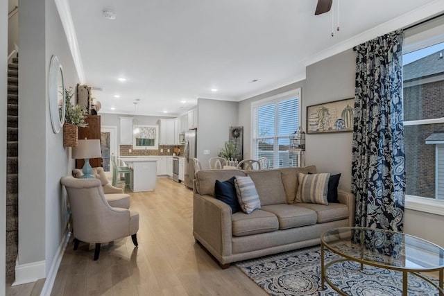 living area with a ceiling fan, baseboards, ornamental molding, stairs, and light wood-style floors