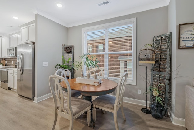 dining area featuring light wood finished floors, visible vents, a healthy amount of sunlight, and crown molding